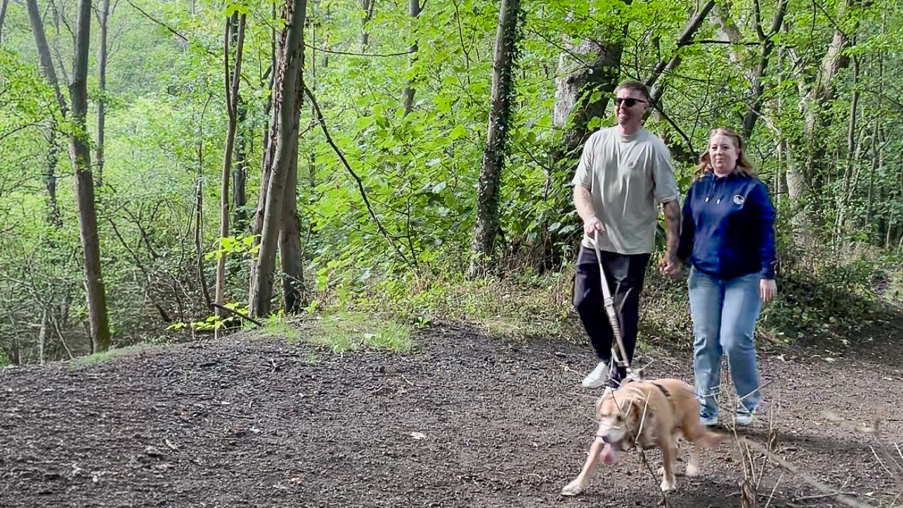 Bex and Dave walking Terra through a green woodland