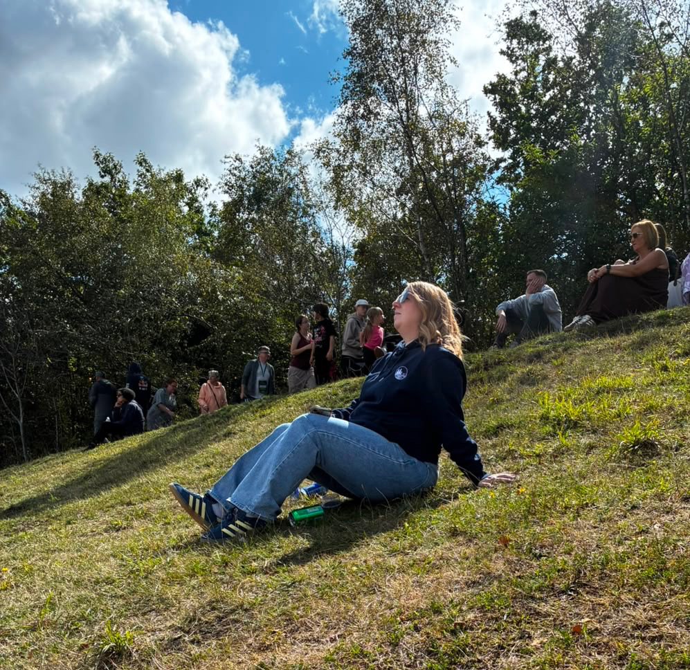 RippleNorth founder sitting outdoors on a grassy hillside wearing the navy Northbound Hoodie