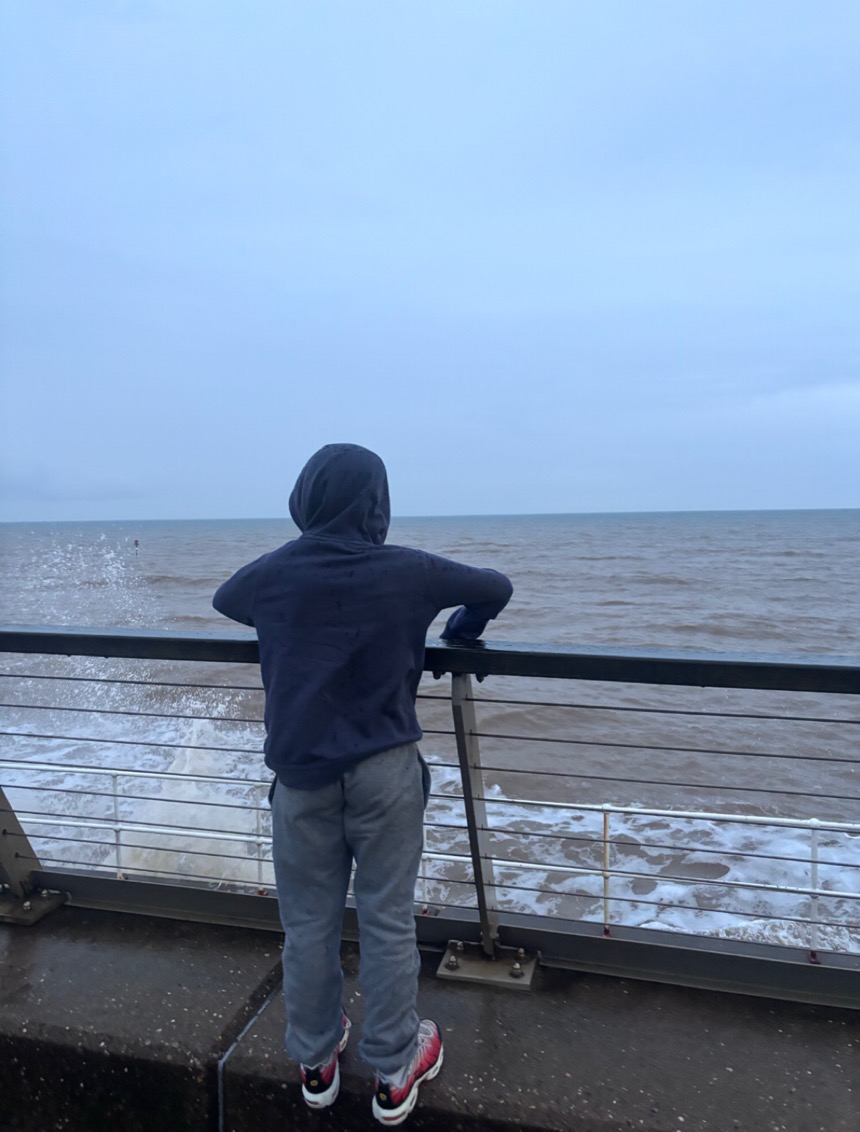 A child watching the waves from a seafront railing